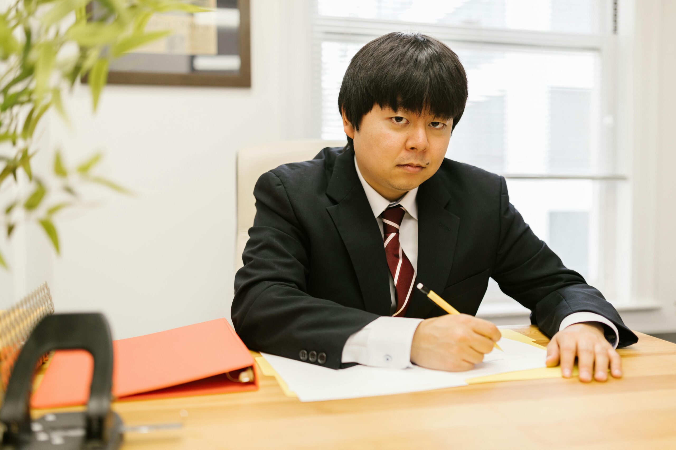 Man in a black suit with a pencil working at a desk in an office setting.